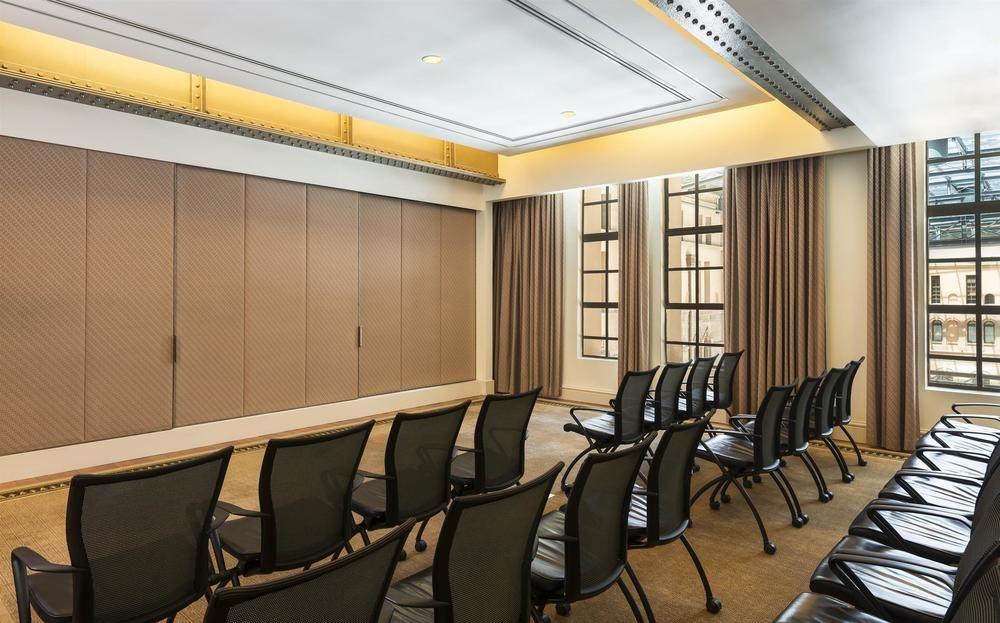 The Fullerton Hotel Sydney Esterno foto The photo shows a modern conference room or meeting space. There are several rows of black chairs arranged facing a wall. The walls appear to have a beige tone with large windows adorned with curtains, allowing natural light to enter. The ceiling is 