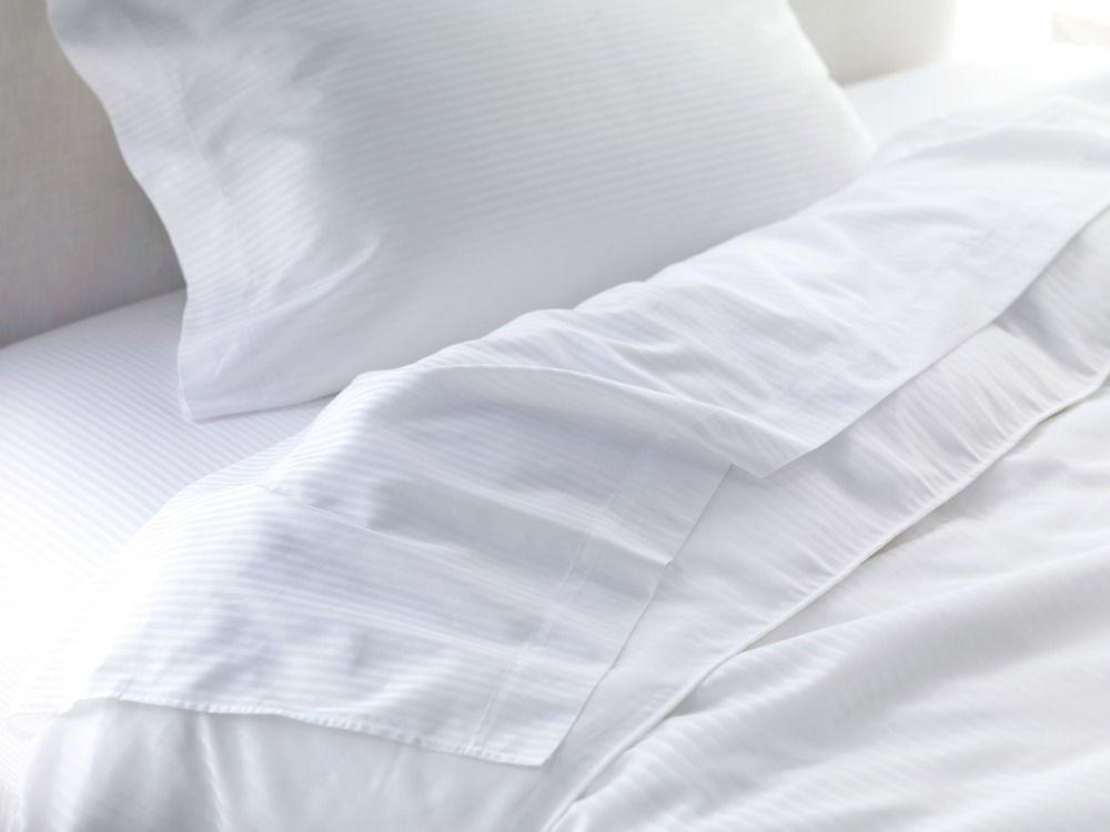 The Fullerton Hotel Sydney Esterno foto The photo shows a neatly made bed with white bedding. There is a white pillow positioned at the top, and a light, textured blanket or duvet partially draped over the mattress, revealing a smooth white fitted sheet underneath. The overall aesthetic is