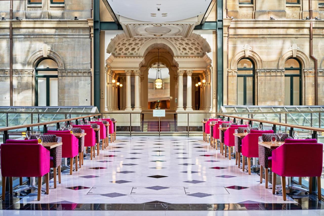 The Fullerton Hotel Sydney Esterno foto The photo shows a stylish and elegant interior of a restaurant or café. There are several tables arranged in a row, each accompanied by bright pink chairs. The flooring features a checkerboard pattern with black and white tiles. In the background, th