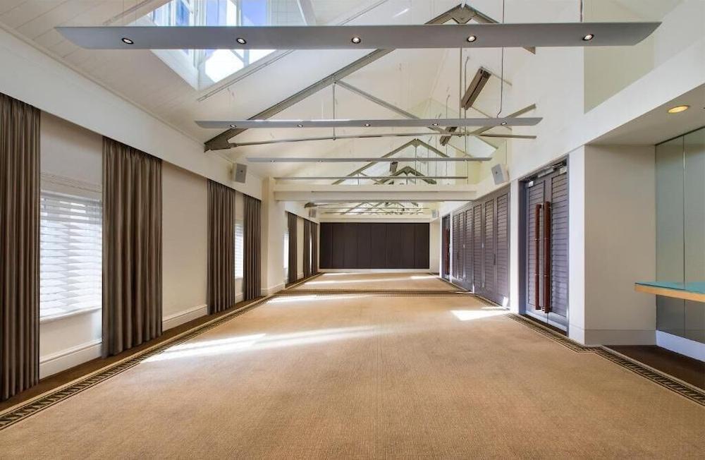 The Fullerton Hotel Sydney Esterno foto The photo depicts a spacious interior room with a high ceiling featuring exposed beams. The flooring appears to be carpeted in a neutral color. Natural light floods the room through large windows and skylights, creating a bright atmosphere. On the si