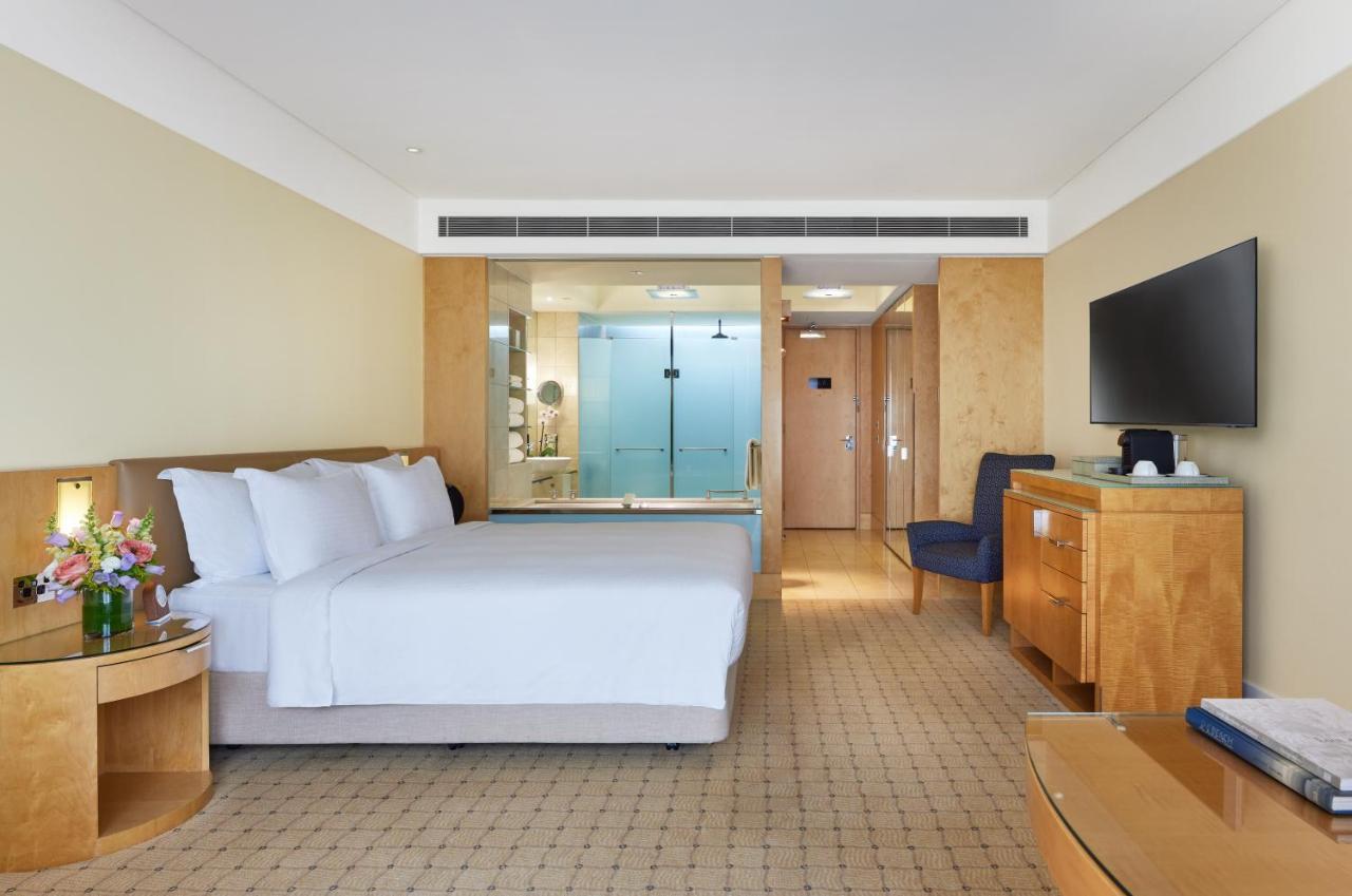 The Fullerton Hotel Sydney Esterno foto The photo depicts a modern hotel room featuring two neatly made beds with white linens. The room has light-colored walls and a warm, inviting atmosphere. On one side, there is a wooden bedside table, and a bouquet of flowers adds a touch of color. A 