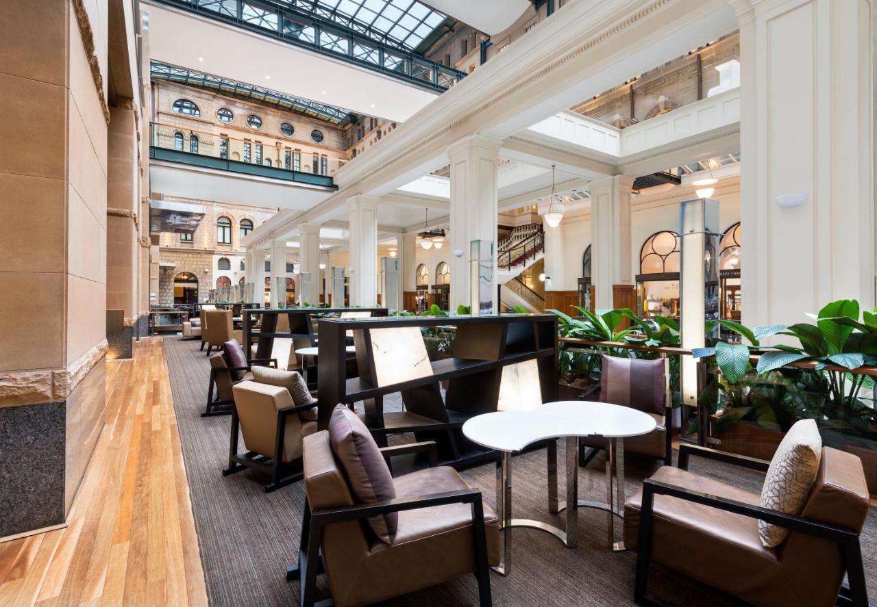 The Fullerton Hotel Sydney Esterno foto The photo depicts a stylish, modern interior space, likely a hotel lobby or lounge area. It features tall ceilings with large windows that allow plenty of natural light to enter. The flooring is a combination of wood and carpet, creating a warm atmos