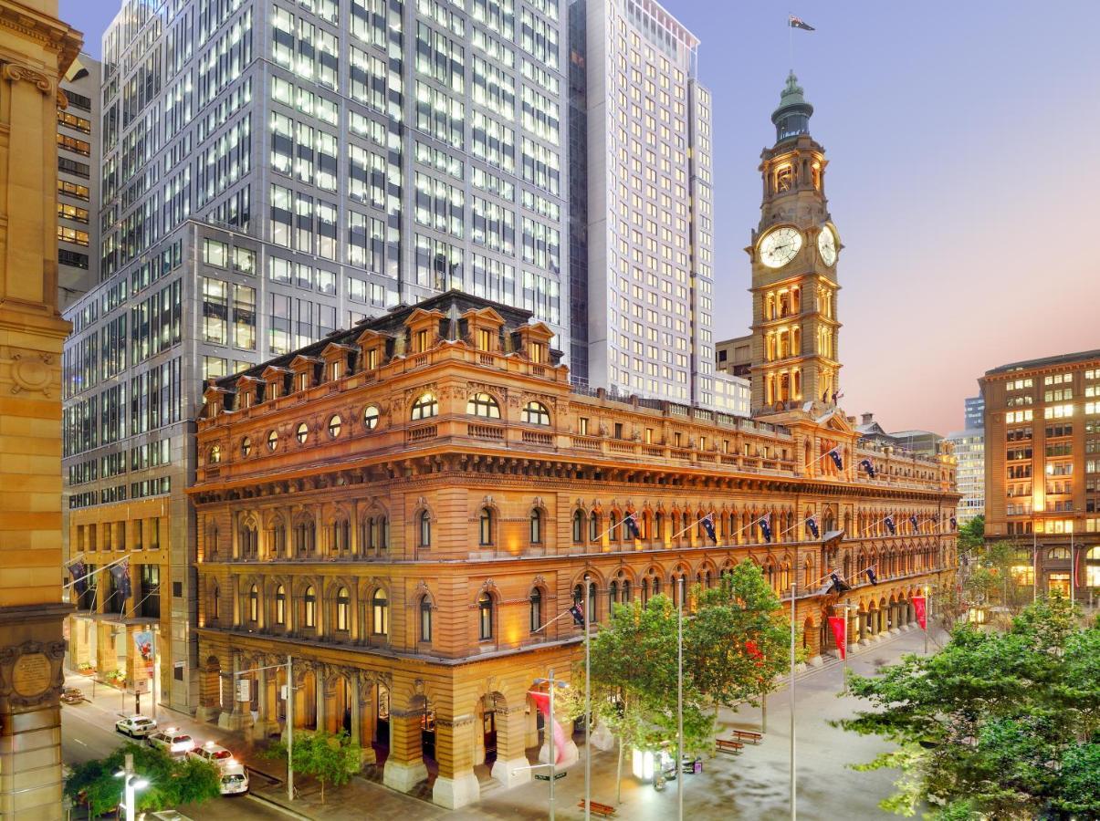 The Fullerton Hotel Sydney Esterno foto The photo depicts a cityscape featuring a historical building with ornate architecture, prominently displaying a large clock tower. This structure is set against the backdrop of modern skyscrapers, highlighting a contrast between classic and contempo